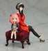 The Spy x Family Anya and Yor PVC Figure features a 15 cm depiction of Anya with pink hair and green toy, and Yor in a red dress on a red cushioned bench, capturing an adorable mother-daughter moment in a sofa sitting pose.