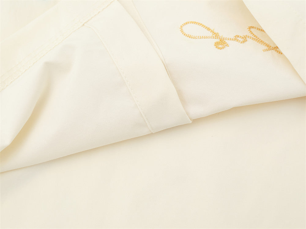 Cream shirt side seam close-up with yellow script embroidery near the hem