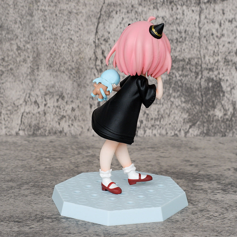 The Spy × Family collection features the Anya Forger Bear Pajamas Figure, a 15cm PVC piece showcasing a character in pink hair, black gown, and red shoes holding a small blue toy. It stands on a textured blue base with a gray backdrop.