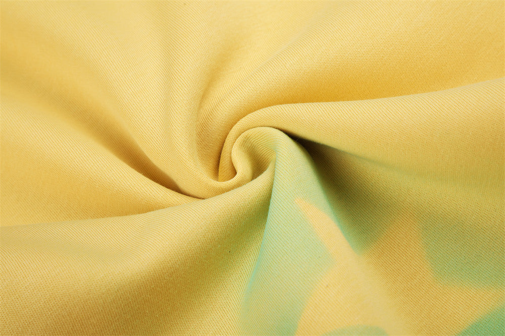 Close-up of yellow sweatpants fabric twist showing green and blue spray-dye accents