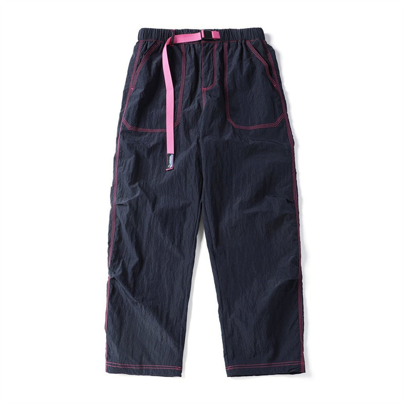 Front view of navy parachute pants with pink contrast stitching, drawcord, and cargo pockets
