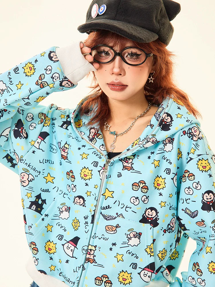 A person with reddish hair and glasses wears a Seakoff Kawaii Cartoon Bear Hoodie in light blue, featuring cartoon characters like stars, suns, playful figures, and bears. They complete their look with a black hat and necklace.