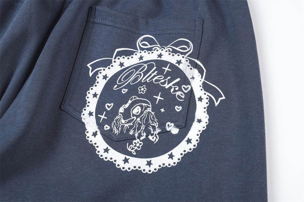 Close-up of back pocket print on navy track pants with star and ribbon design
