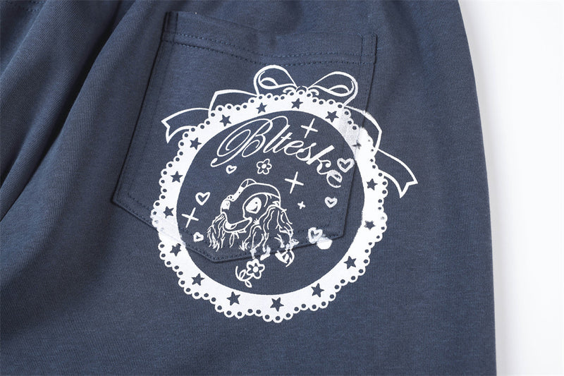 Close-up of back pocket print on navy track pants with star and ribbon design
