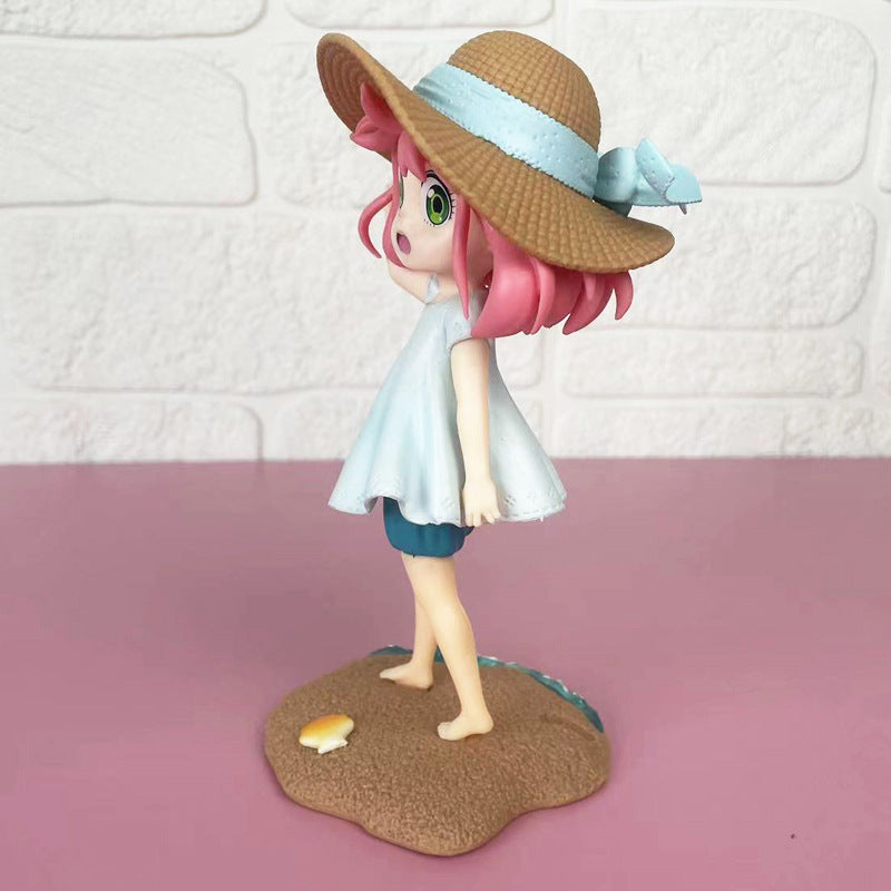 The Anya Forger Beach Day PVC Figure from the Spy × Family Summer Collection features a pink-haired girl in a large straw hat and light blue dress, standing on a sandy base with a shell, set against a white brick wall and pink surface.