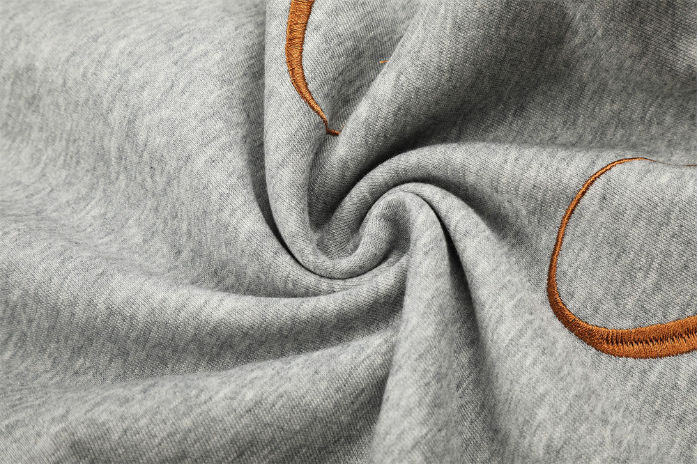 Close-up of heather gray sweatpants fabric with brown embroidery and gathered folds