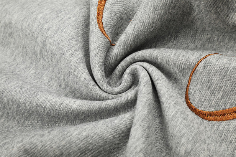 Close-up of heather gray sweatpants fabric with brown embroidery and gathered folds