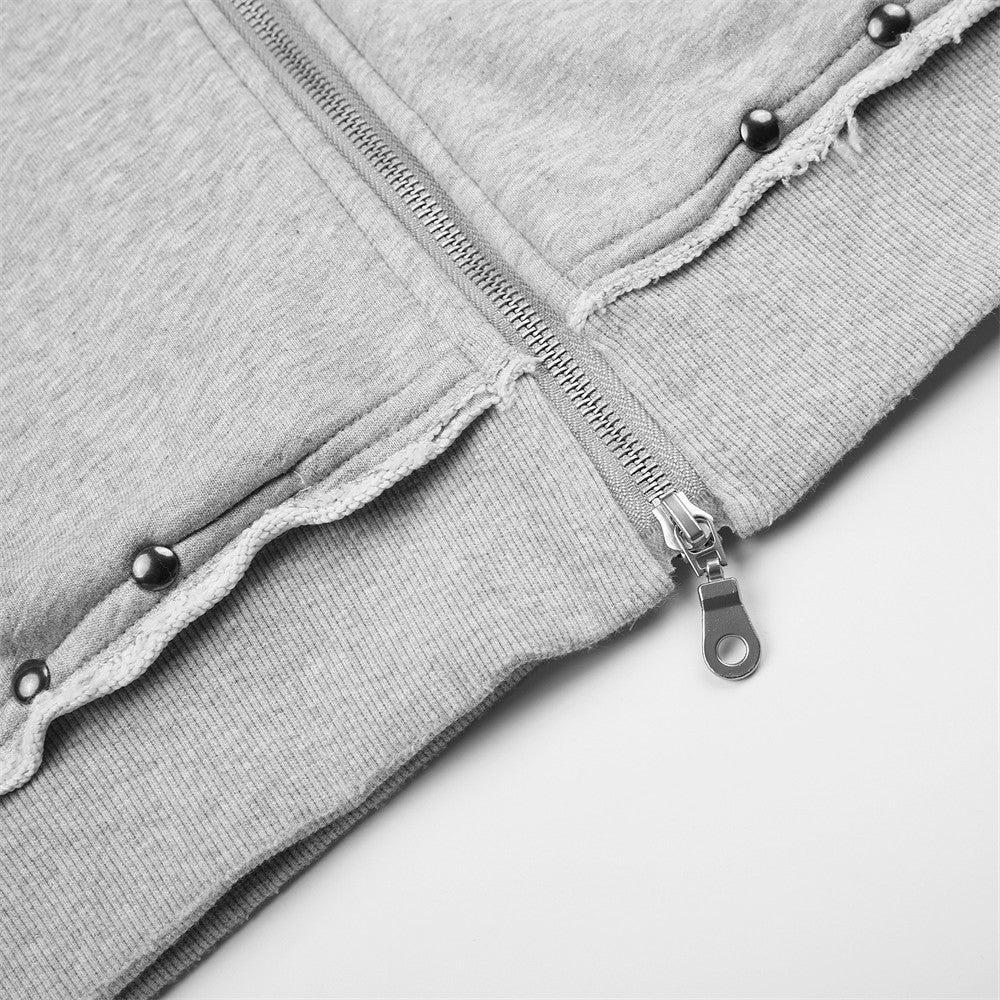 Close-up of light gray hoodie front hem with zipper pull, ribbed trim and studded distressing