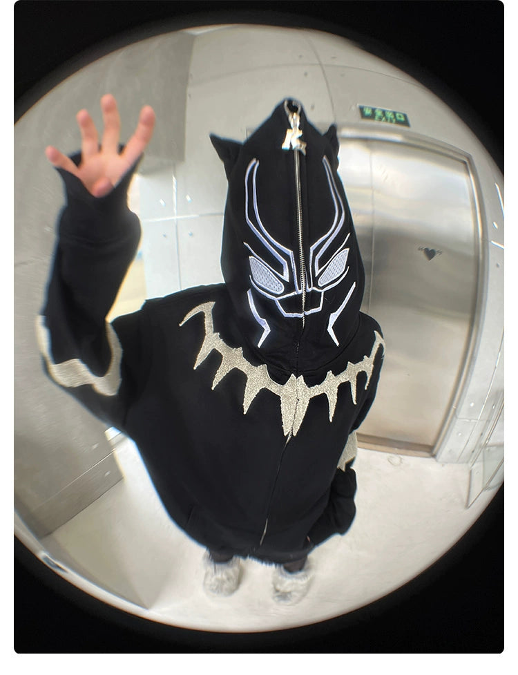 Sporting the Seakoff Black Panther-Inspired Hoodie, crafted from 400GSM cotton with a white superhero mask and ear design, they pose indoors raising a hand. A fisheye lens adds a unique style to this oversized streetwear look.