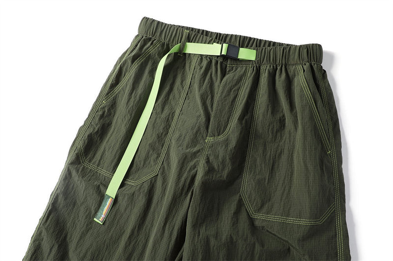 Close-up of olive parachute pants showing front cargo pockets, bright green drawcord, and crinkled fabric