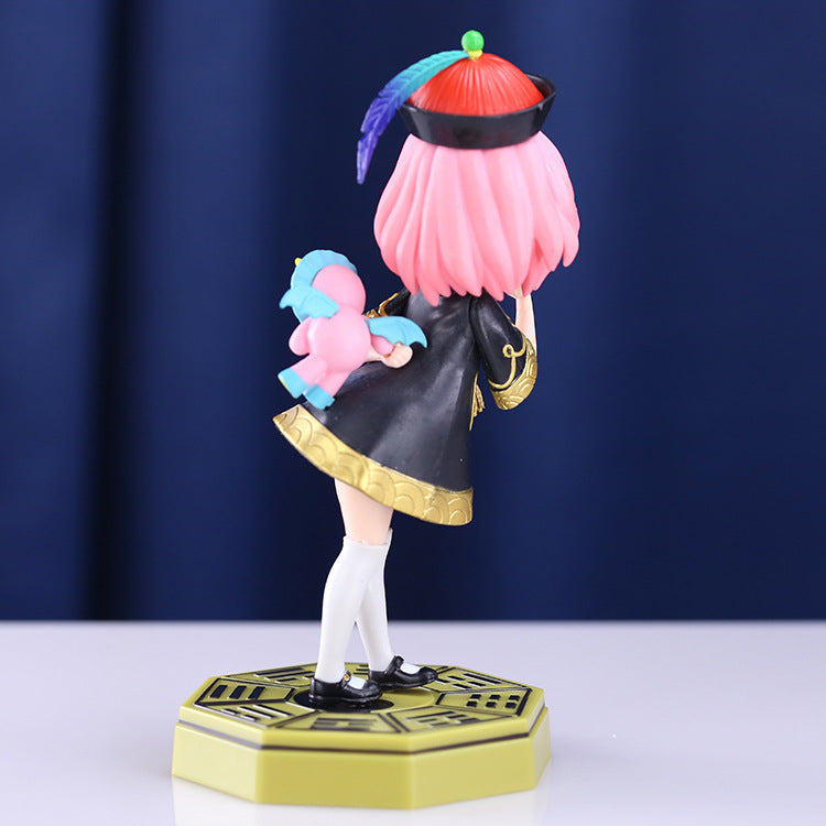 The Spy × Family Anya Forger PVC Figure, 18 cm, captures Anya in a school uniform with pink hair and a decorative cap, hiding a toy behind her. She stands poised on a hexagonal base against a dark blue backdrop.