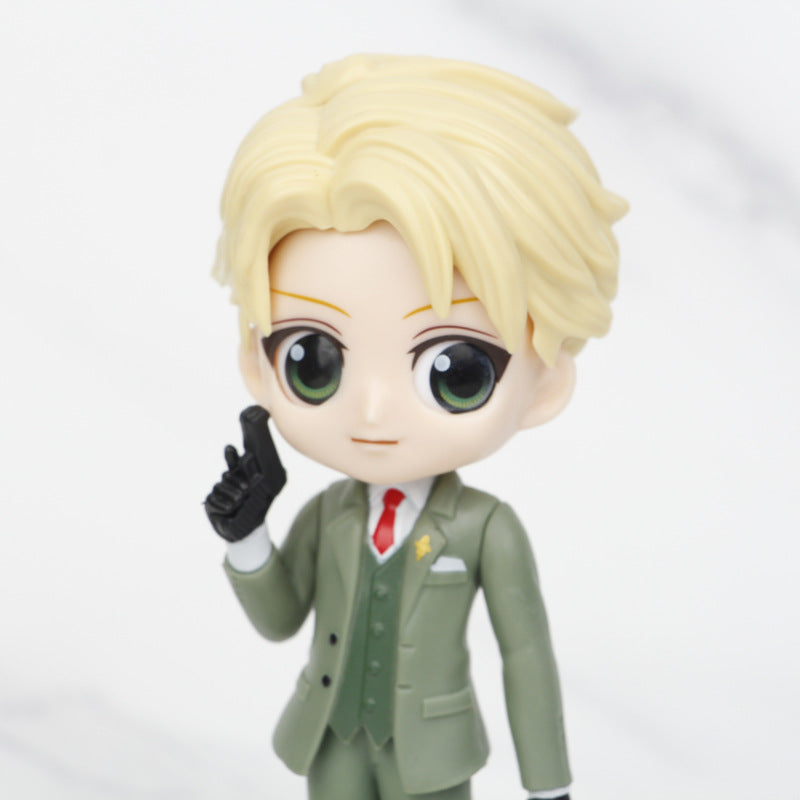 From the Spy × Family Complete Set featuring Anya, Loid, and Yor PVC Figures - 15cm, a chibi-style figure of Loid with blond hair and playful pose wears a green suit with a white shirt and red tie, set against a marble-textured background.