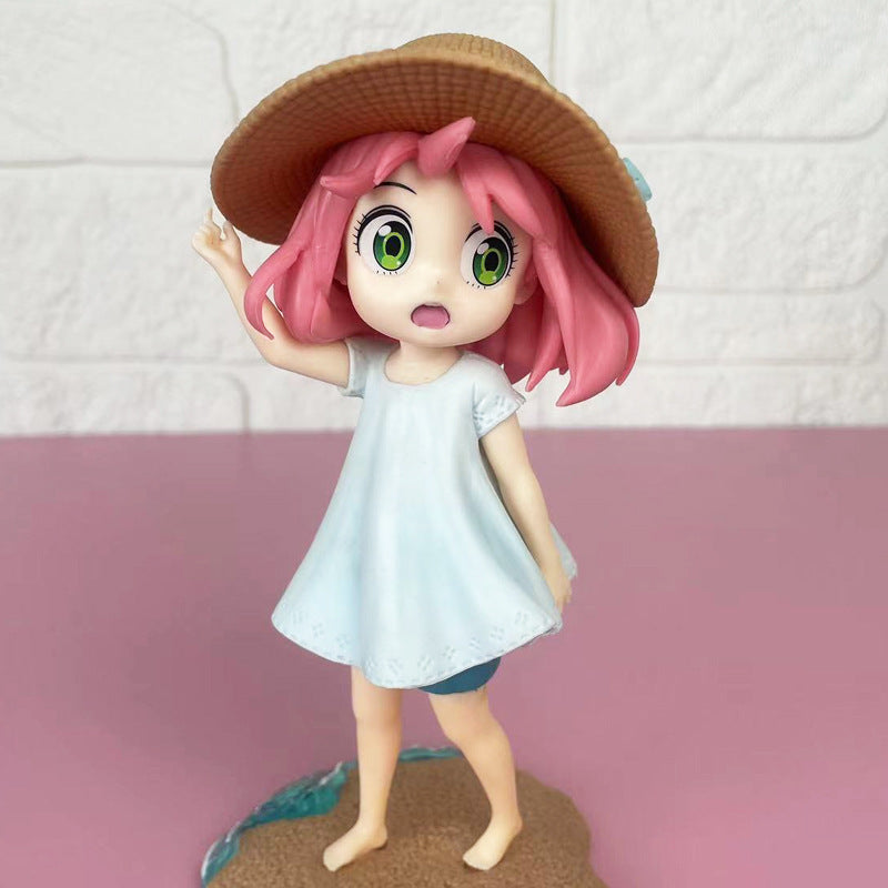 The Anya Forger Beach Day PVC Figure from the Spy × Family Summer Collection features a pink-haired girl in a wide-brimmed straw hat and light blue dress, standing on a small base. Her surprised expression as she touches her hat is set against a pink surface with a white textured wall.