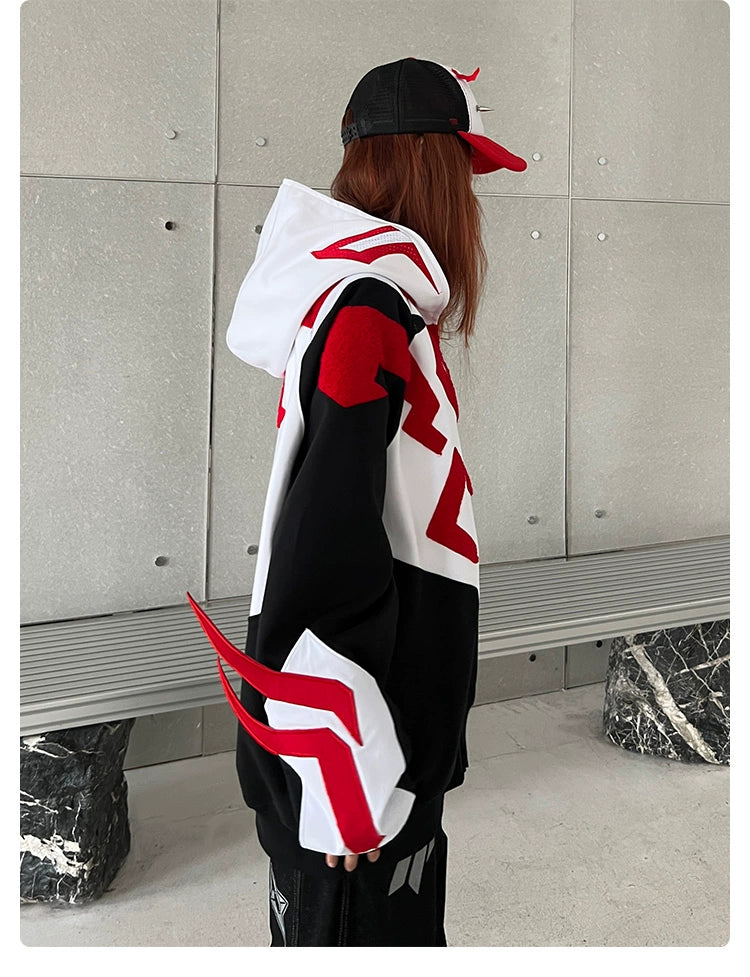 Wearing a Seakoff Superhero-Inspired Hoodie in black, white, and red, perfect for streetwear fans, someone with long hair stands sideways by a concrete wall. They also wear a red and black cap. A bench and dark stone block are seen in the background.