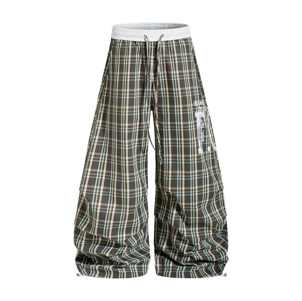 Oversized brown plaid wide-leg parachute pants with white elastic waistband and distressed letter graphics, front and back vi