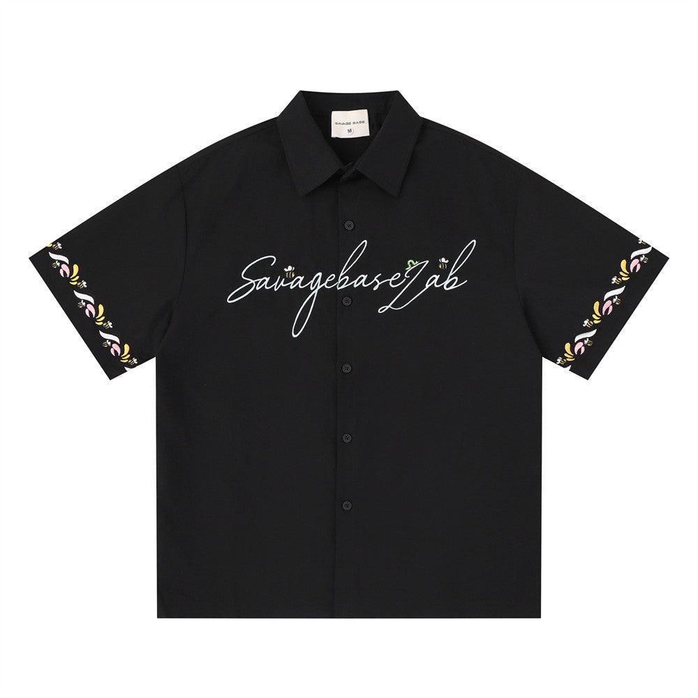 Men's oversized short sleeve button-up shirt in black with cursive Savagebase Lab chest logo and floral embroidery sleeve tri