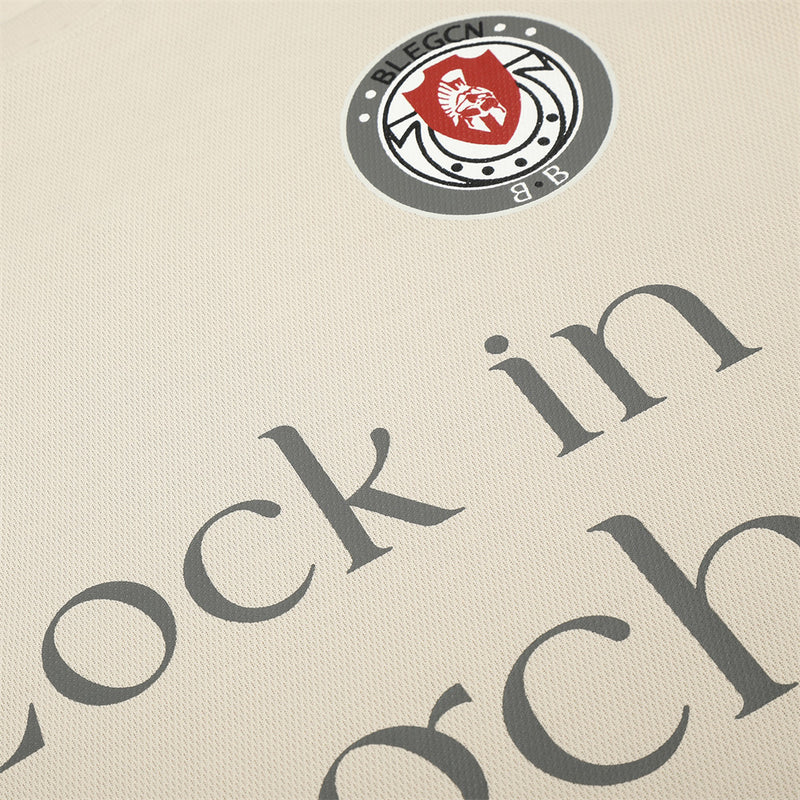 Beige tee chest detail with crest patch and diagonal Lock in Blegchn text