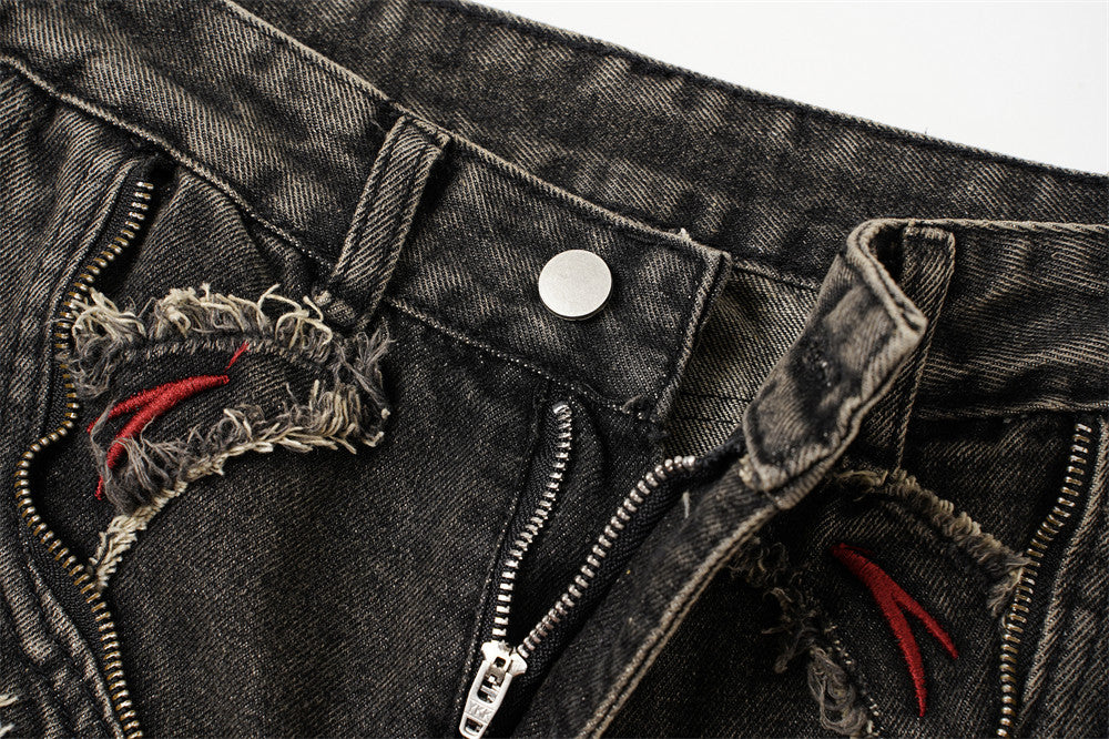 Close-up of the front waist showing button, zipper, frayed denim patches, and red embroidery