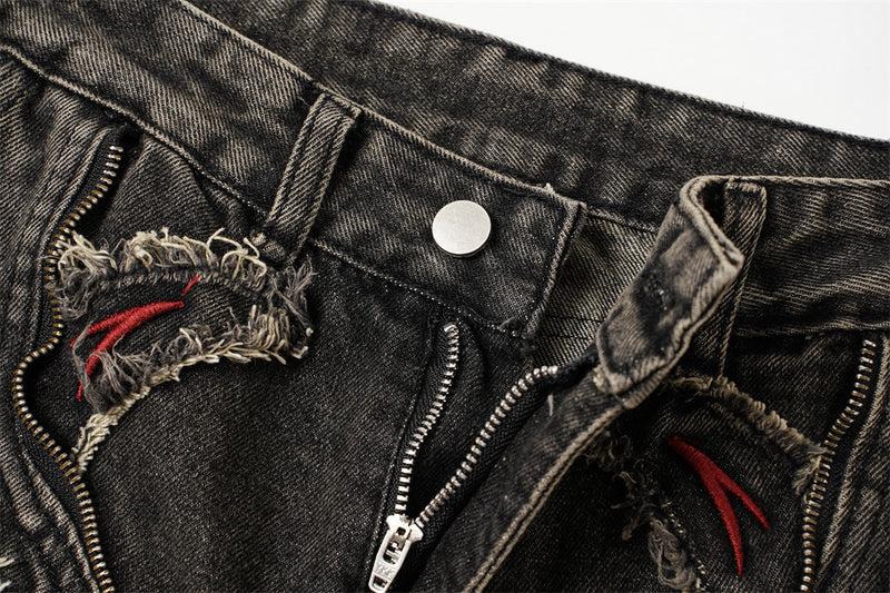 Close-up of the front waist showing button, zipper, frayed denim patches, and red embroidery