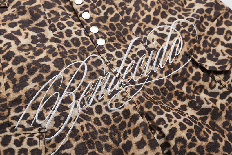 Close-up of leopard print shorts front with metal snaps and large script graphic across the waist