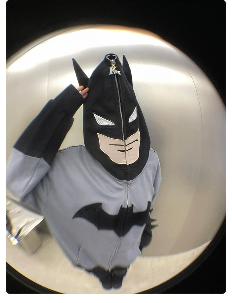 A person wearing a Seakoff Batman-Inspired Hoodie poses against a metallic background. This 400GSM oversized grey and black zip-up superhero sweatshirt features a prominent Batman logo, complete with mask and ears. A fisheye lens adds a unique perspective to the image.