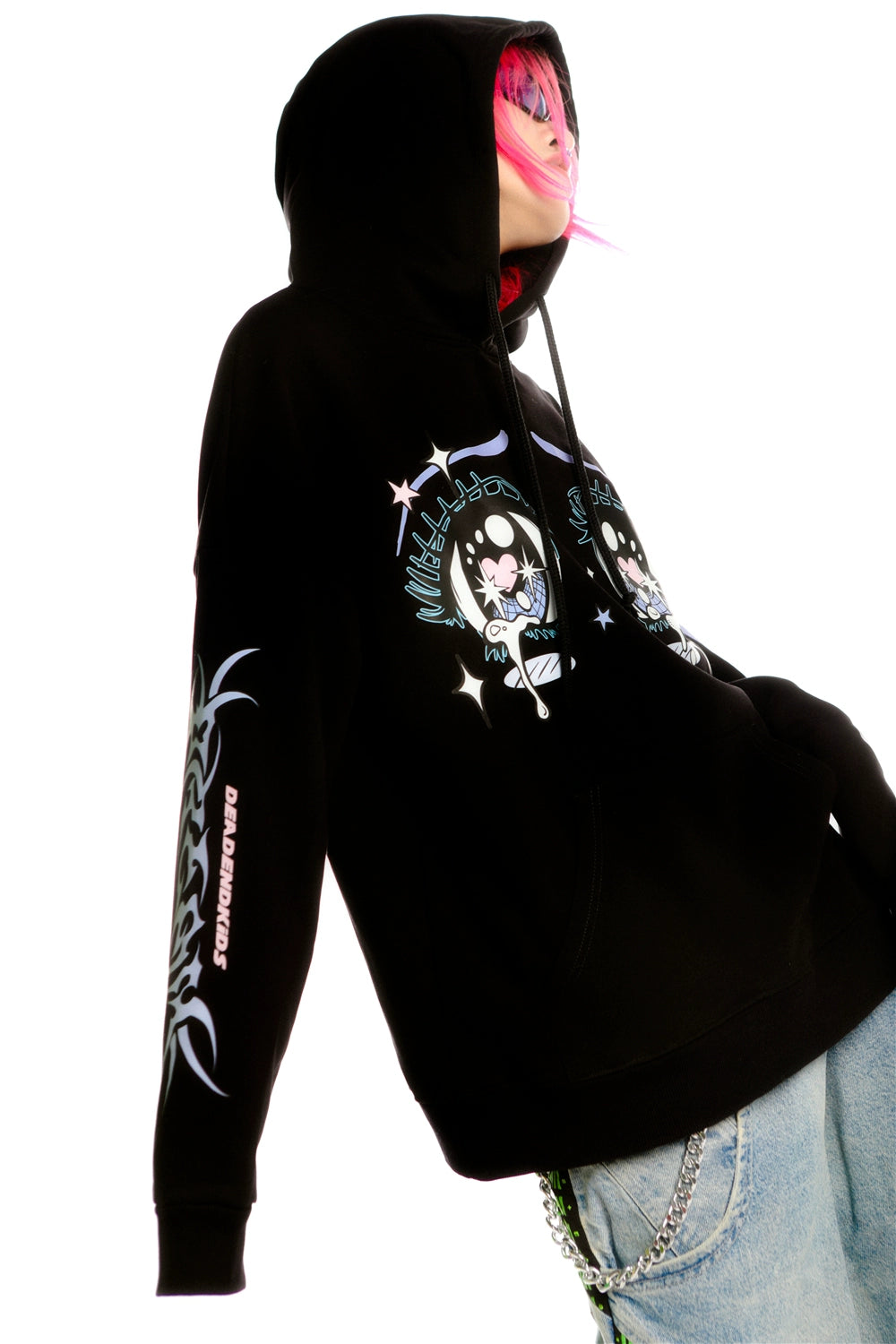 A person with pink hair wears the Seakoff Kawaii Aesthetic Crying Eyes Hoodie, a black pullover featuring pastel and dark anime graphics, embodying streetwear fashion. They stand against a white background wearing denim jeans with a chain accessory visible.