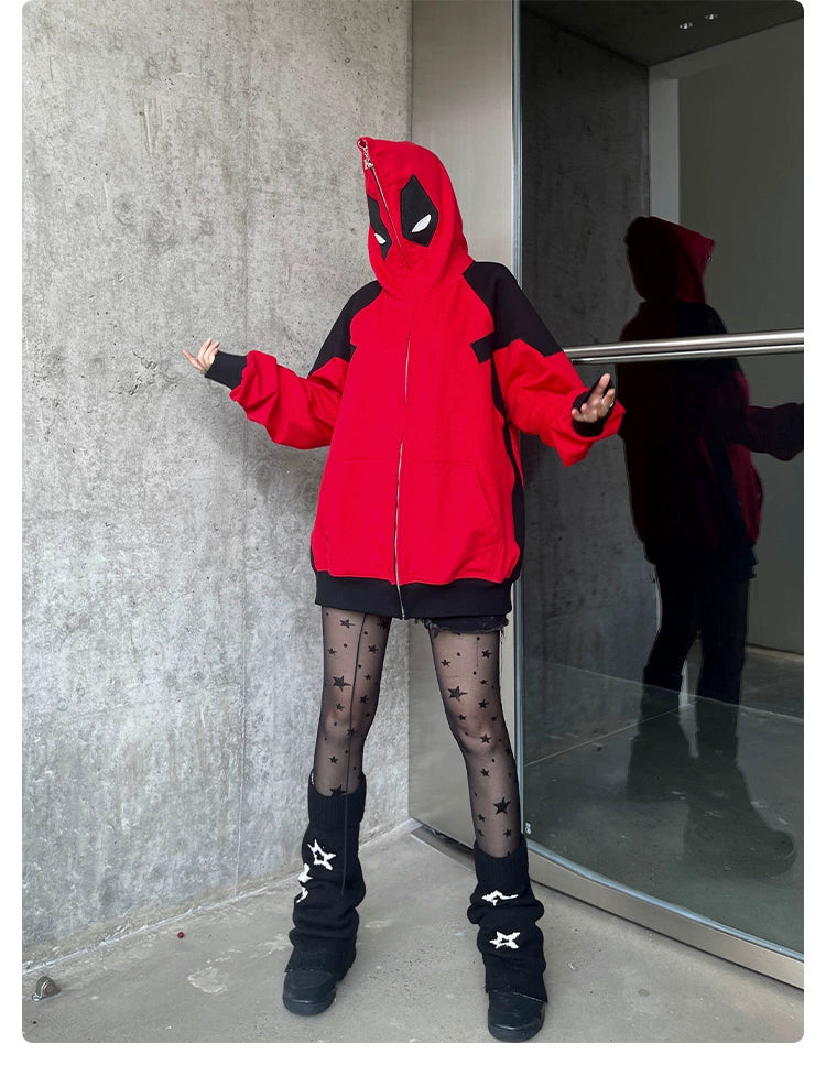 A person wears a Seakoff Deadpool-Inspired Hoodie, an oversized red and black 400GSM zip-up superhero sweatshirt, paired with black star-patterned tights and leg warmers. Standing by a concrete wall and glass doors, their reflection embodies streetwear style.