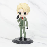 The Spy x Family Complete Set features chibi-style PVC figures of Anya, Loid, and Yor. The Loid figure showcases blond hair, a green suit, red tie, and black gloves, standing on a round black pedestal with an upward-pointing finger. Perfect for anime collectors and Spy × Family fans.