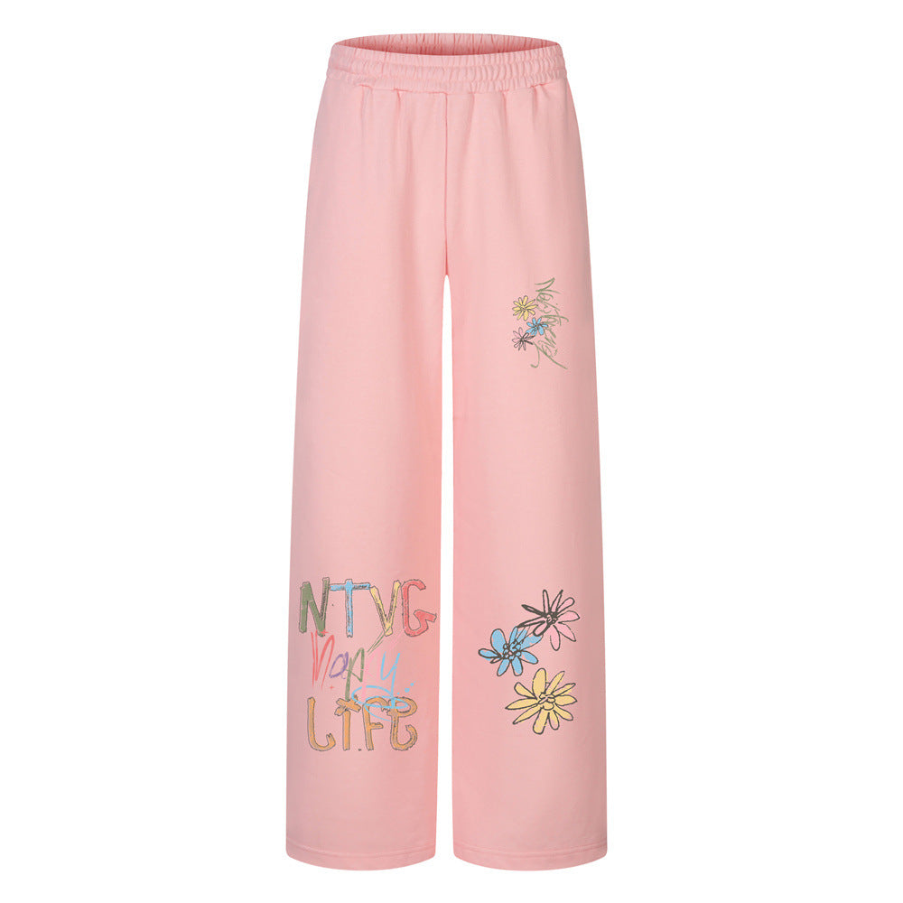 Sweatpants mit weitem Bein in Rosa, mit Graffiti-Schriftzug und buntem Gänseblümchen-Print am Bein