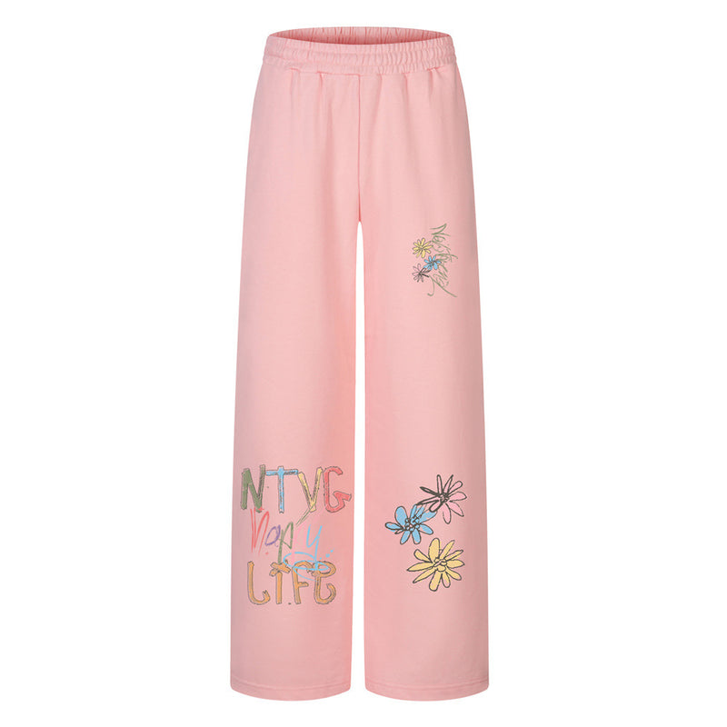 Sweatpants mit weitem Bein in Rosa, mit Graffiti-Schriftzug und buntem Gänseblümchen-Print am Bein