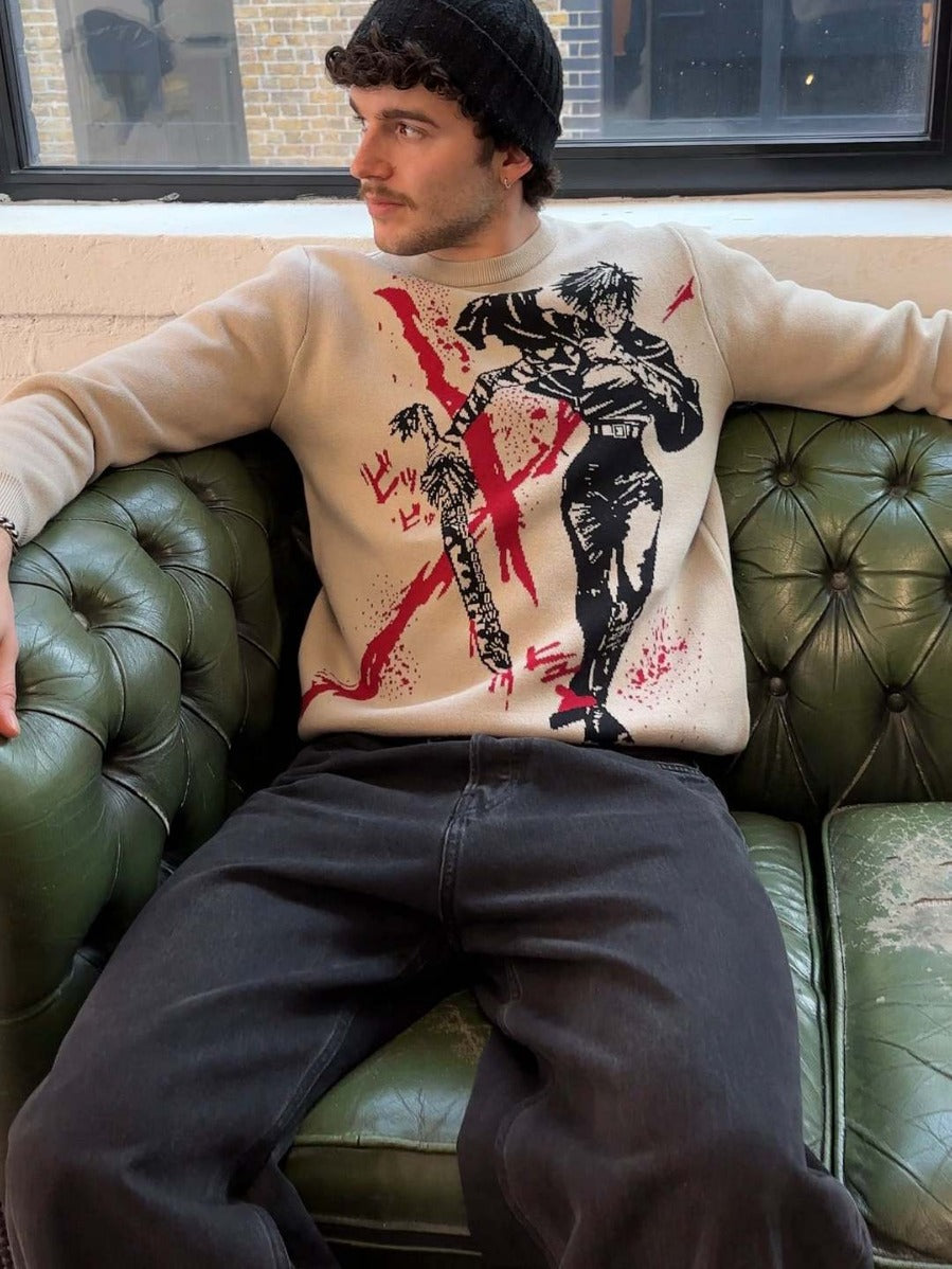 Wearing a Premium Maki Zenin-Inspired Knit Sweater – Jujutsu Kaisen Bloody Spear Jacquard Design and black pants, a person sits on a green leather sofa. A black beanie adorns their head as they gaze aside, with a window revealing a brick building that adds an urban touch to this anime streetwear ensemble.