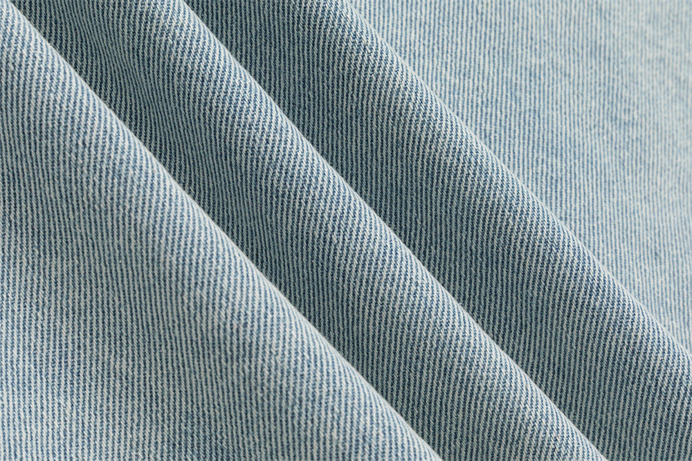Close-up showing the woven light wash denim texture and diagonal fabric folds