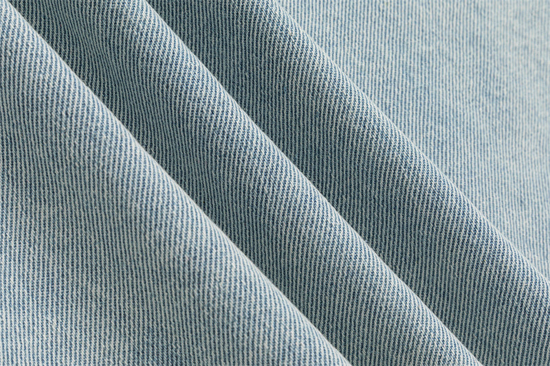 Close-up showing the woven light wash denim texture and diagonal fabric folds