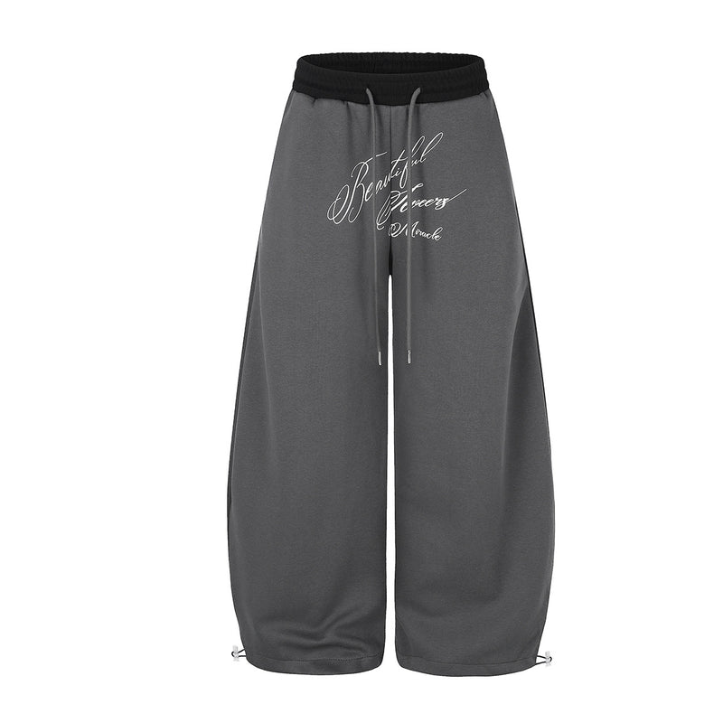 Pantalon de survêtement gris à jambes larges avec imprimé à écriture cursive et ceinture élastique noire contrastante, vue de face