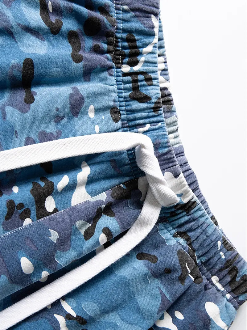 Close-up of Men's Blue Camo Drawstring Shorts—relaxed fit cotton camouflage shorts with an elastic waistband and white drawstrings, laid flat on a white background. Ideal for men's streetwear style.