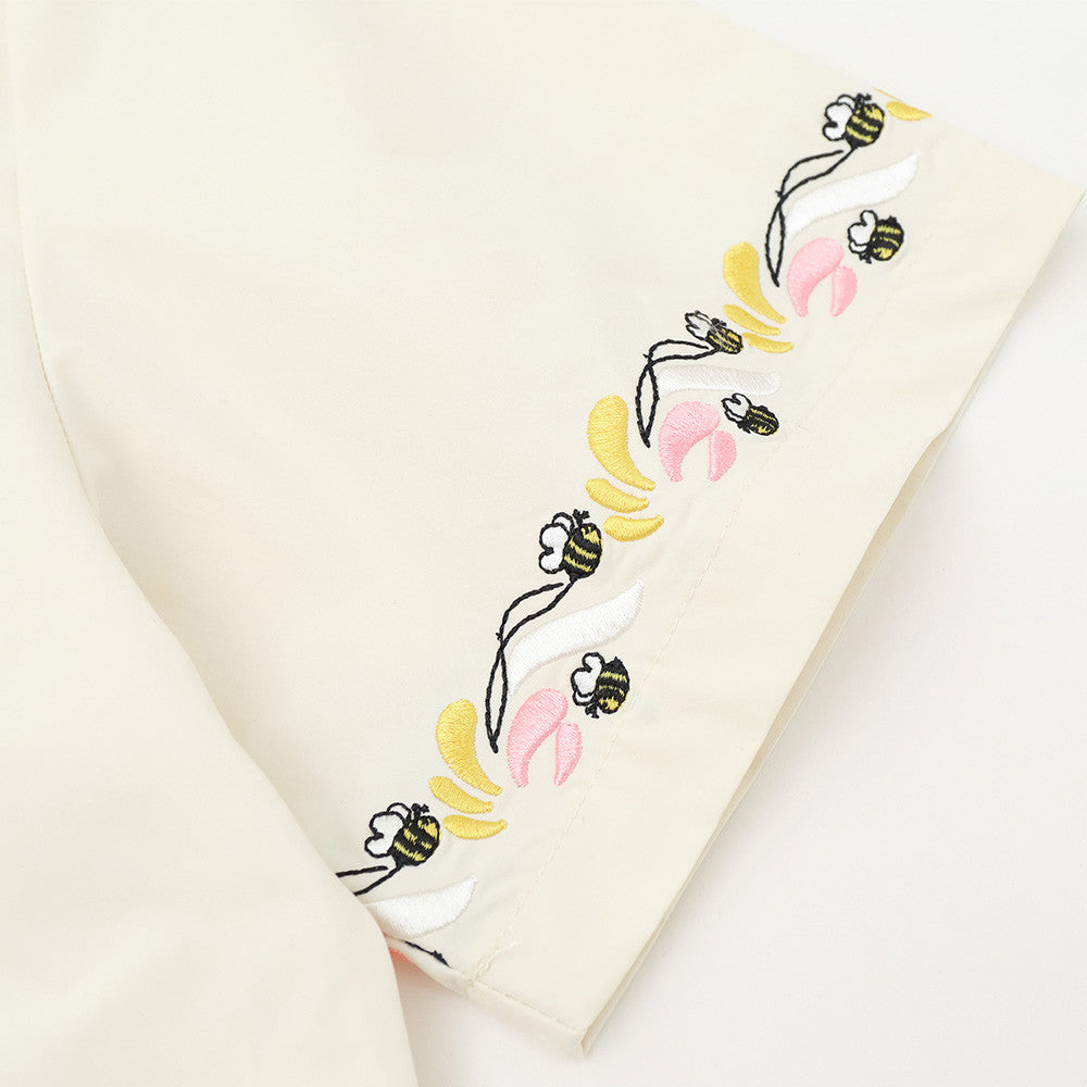 Close-up of cream shirt sleeve hem with floral and bee embroidery