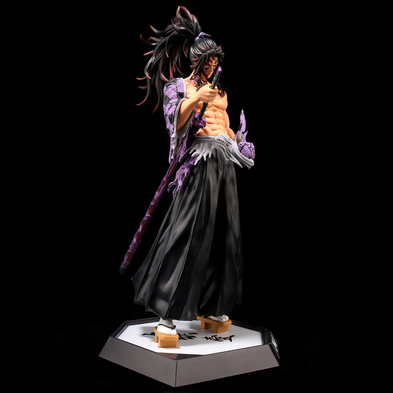 The Kokushibo Demon Slayer Figure is a 31CM PVC action collectible for Kimetsu no Yaiba fans, featuring the long-haired anime character with a sword in a dark robe with patterned sleeves. It stands on a hexagonal base with Japanese characters on a black background.