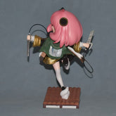 The 17.5CM Anya Forger Cosplay Figure from Spy × Family features a girl with pink hair and a green jacket, brandishing swords while balancing playfully on one leg atop a tiled base. Her hair partially obscures her face, making it an eye-catching anime collectible.