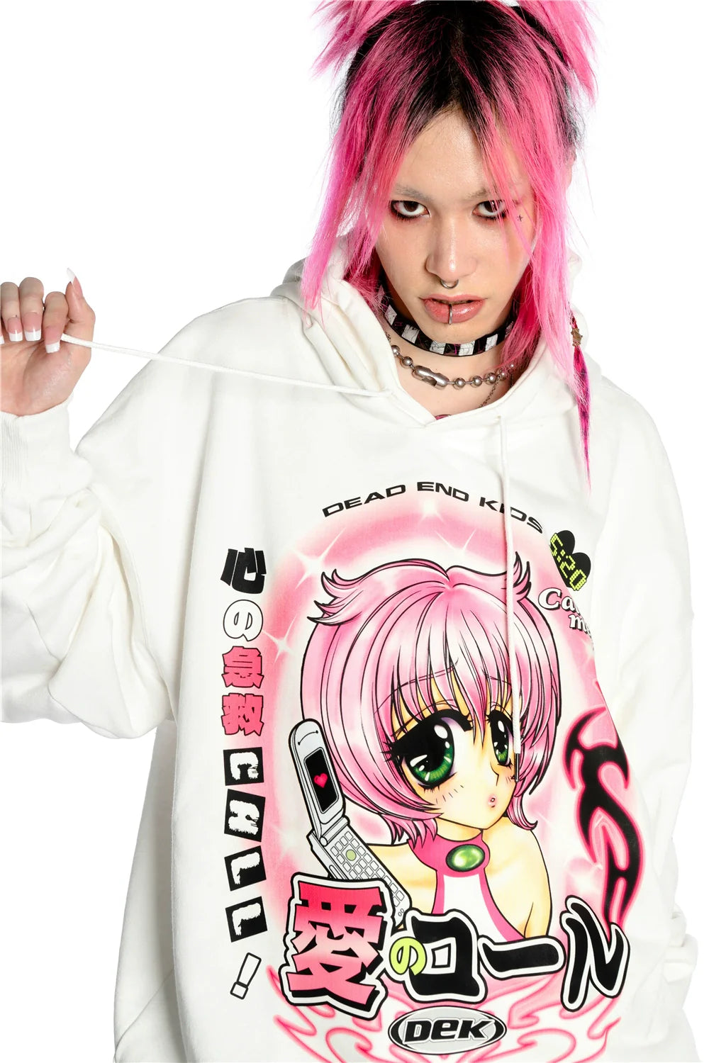 Sporting pink hair and a black choker, an individual embraces the kawaii aesthetic with Seakoff's Y2K Aesthetic Anime Hoodie featuring a retro manga girl graphic. Holding one hoodie string, their intense expression completes the blend of Y2K vibes and Japanese text style.
