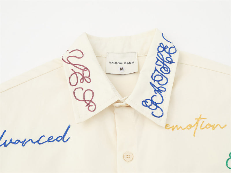 Cream shirt collar close-up with blue and pink script embroidery and button placket