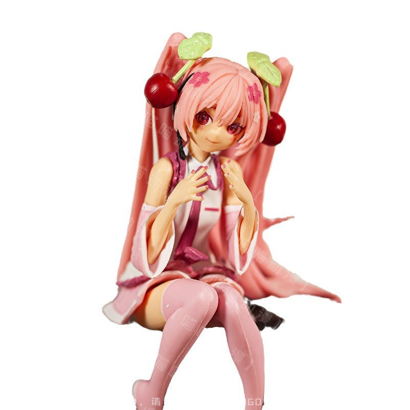 The Hatsune Miku Cherry Sitting Pose 11cm PVC Figure captures the anime character in a pink outfit, long pink hair adorned with cherries, sitting gracefully with hands near the chest and a neutral expression.