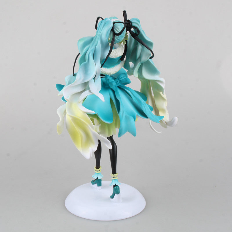 The Hatsune Miku 1/7 Scale 28cm PVC Figure showcases the Vocaloid character in an elegant pose. Her turquoise hair flows beautifully, complemented by a blue, white, and yellow dress with a charming waist bow. She stands on a white circular base against a gray backdrop.