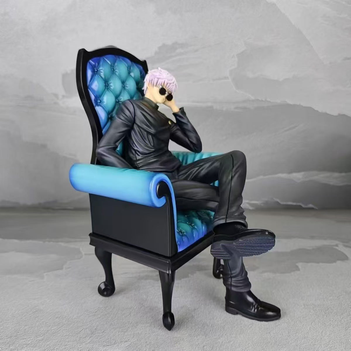 The Jujutsu Kaisen Satoru Gojo &amp; Suguru Geto Sitting Posture PVC Figure Set features a 24 cm Satoru Gojo in a sleek black outfit with short white hair and sunglasses, casually posed in a black and blue armchair against a gray textured background.