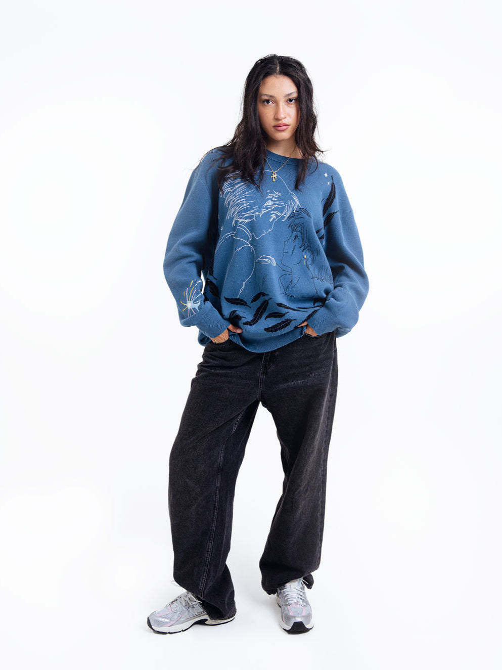 A person with long dark hair stands against a white background, wearing Seakoff's Premium Howl's Moving Castle-Inspired Knit Sweater featuring the Howl & Sophie Starry Jacquard Design, along with loose black pants and white sneakers. With hands in pockets, they gaze forward confidently.