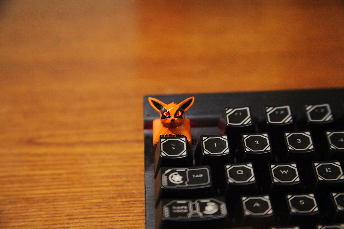 A small, orange Naruto Kurama Nine-Tails Fox chibi-style keycap with large ears sits on a black keyboard, nestled between wooden-surfaced keys above Cherry MX switches.