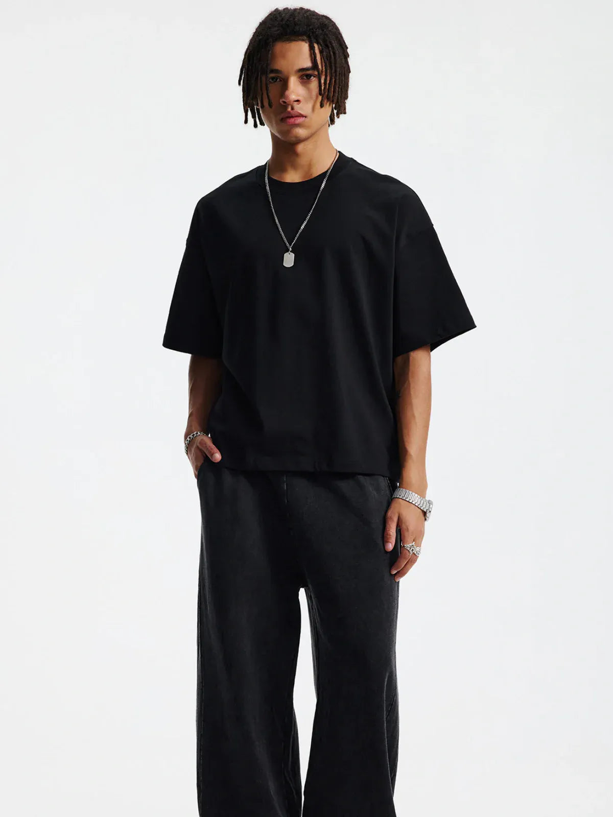 Wearing the Custom Anime Character Black T-Shirt - Personalized 230GSM 100% Cotton Tee, a person with short dreadlocks and silver jewelry poses in loose black pants against a plain white background.