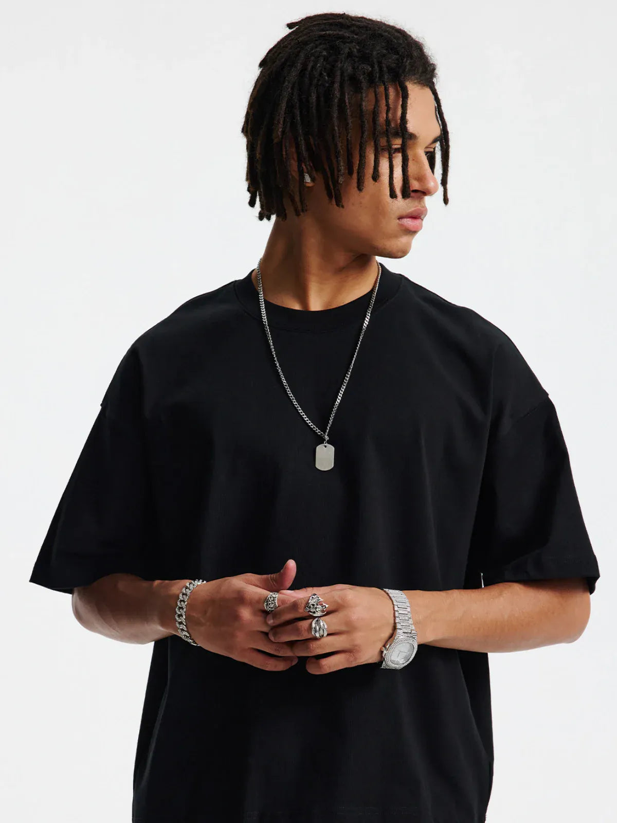 A person in a Custom Anime Character Black T-Shirt—Personalized 230GSM 100% Cotton Tee—paired with a silver chain, bracelets, watch, and rings stands against a plain white background, looking to the side.