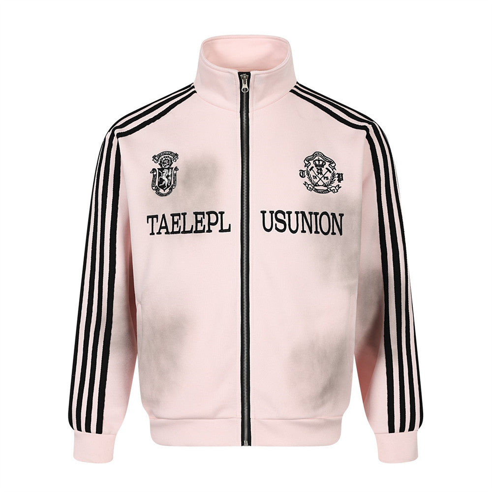Zip-up track jacket in blush pink with black stripe sleeves, embroidered chest crests, and distressed spray-wash finish