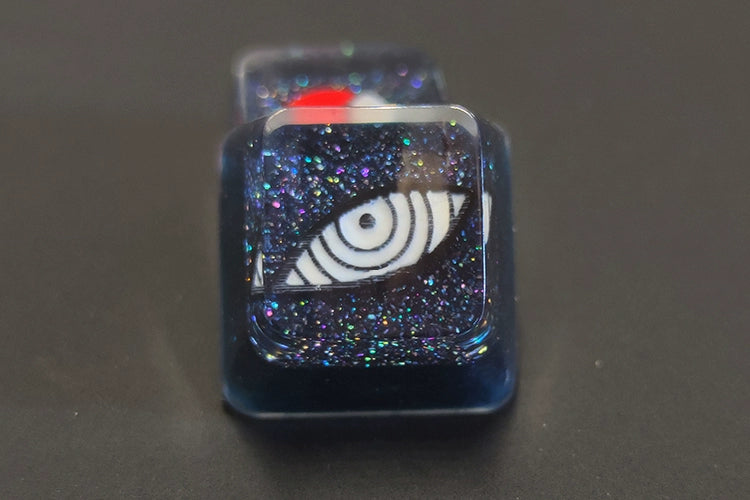 Check out the Naruto Symbols Keycap Set, featuring a resin keycap with a white spiral on a dark glittery background. The transparent layer creates an illuminated effect with a red dot, making it perfect for enhancing your setup against a plain black backdrop.