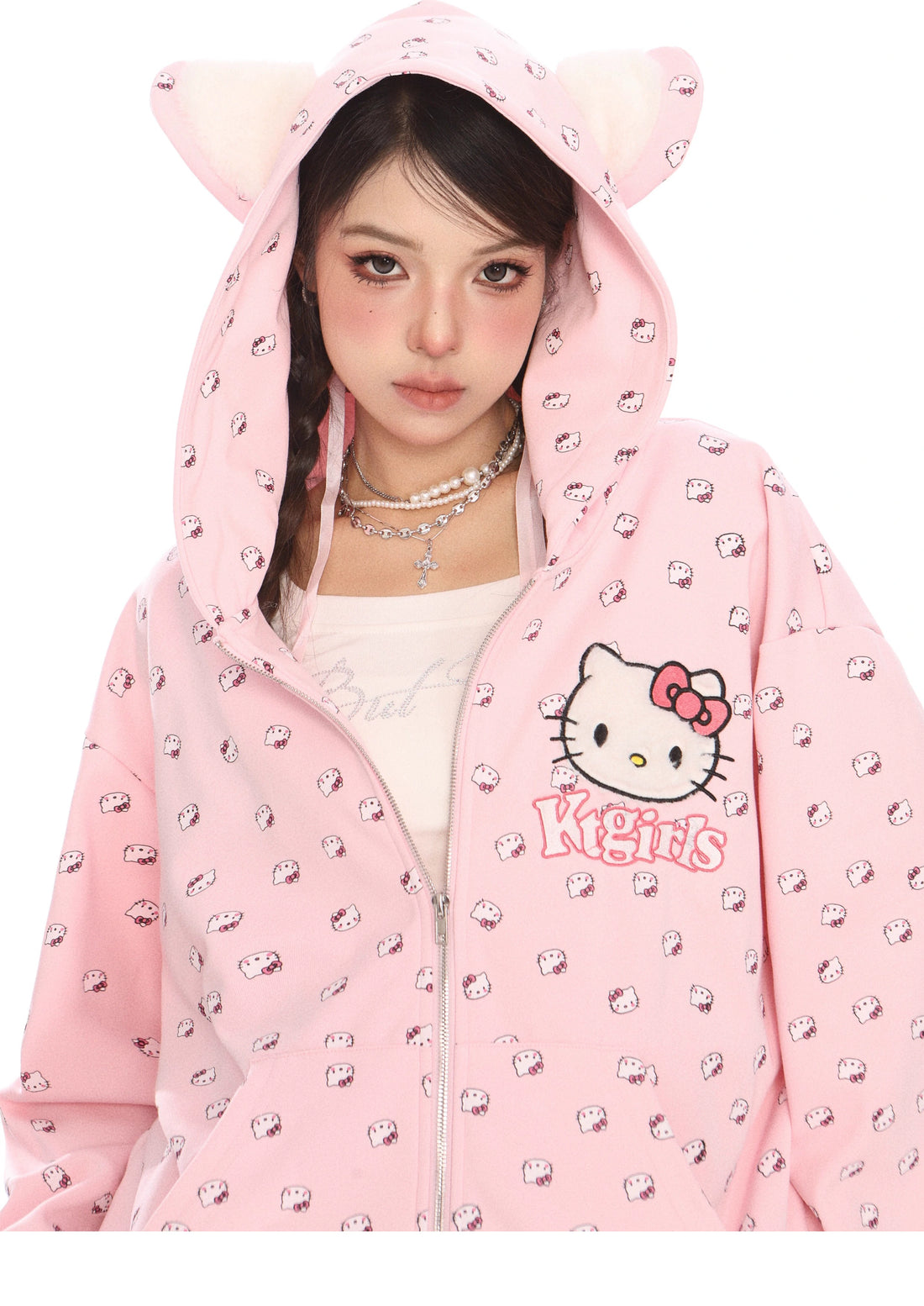 A person wears the Seakoff Hello Kitty Pink Kawaii Hoodie, an oversized zip-up complete with a cat ear hood and all-over Hello Kitty print. Their long hair is braided and complemented by layered necklaces.